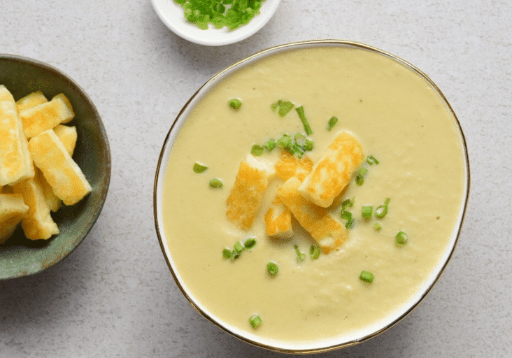 thermomix cauliflower soup in bowl topped with halloumi and chives. White background. Bowl of halloumi and bowl of chives next to soup.