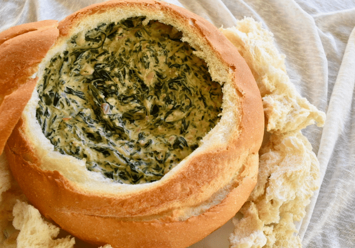 thermomix spinach cob loaf dip in cob loaf. Cream background with chunks of crusty bread around