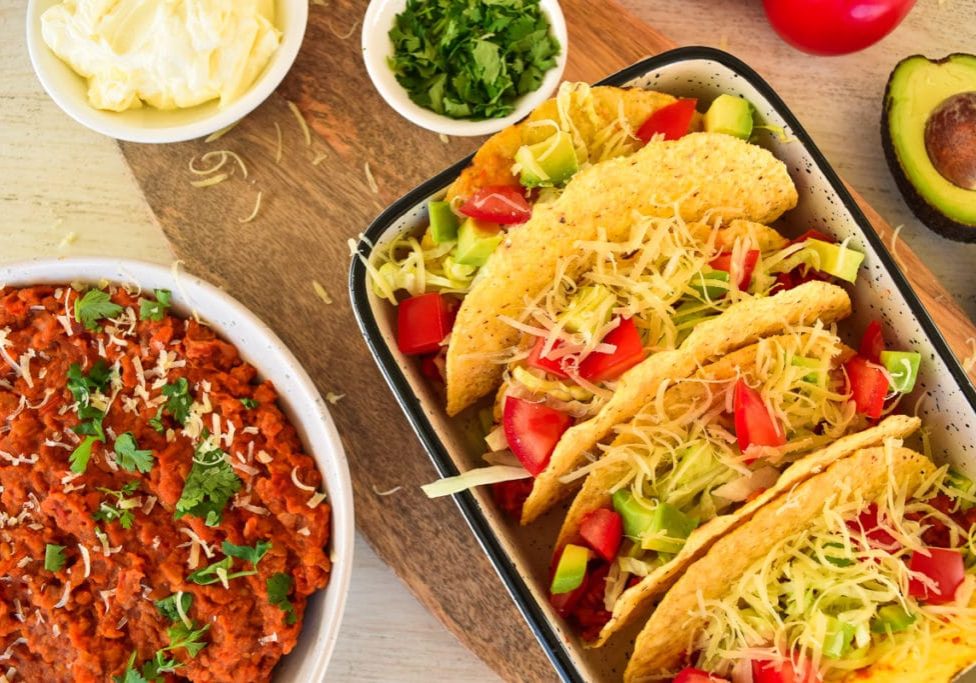 plate of tacos, bowl of taco filling next to it with other ingredients around