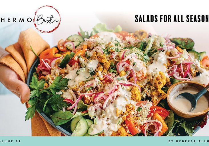 Salad on large platter being held with one hand also holding orange cloth, person in background wearing light blue apron