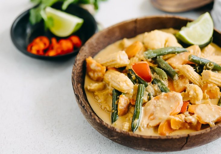 Brown bowl filled with thermomix satay vegetables grey table black bowl with chilli and lime behind