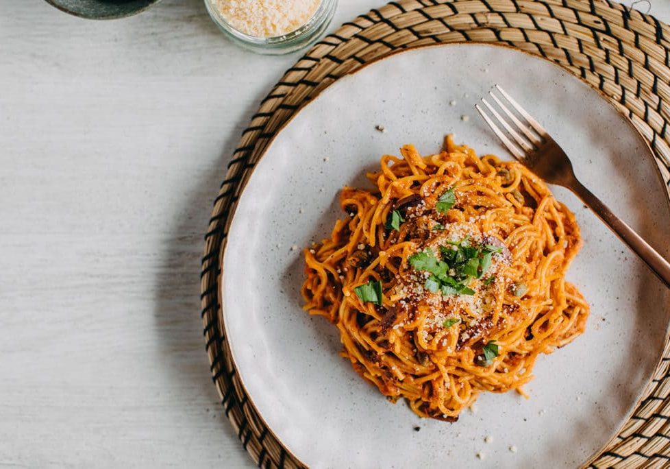 Spaghetti alla Puttanesca flexible thermomix meals, on a plate on woven placemat and light coloured table